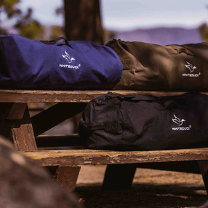 White Duck Outdoors Hoplite Canvas Duffel Bag blue black and olive on bench