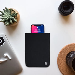 Picture of a Cell phone black canvas X-large privacy protection 4.5 x 6.5 Bag with a cellphone inside it beside a cup, plant, and airpods.