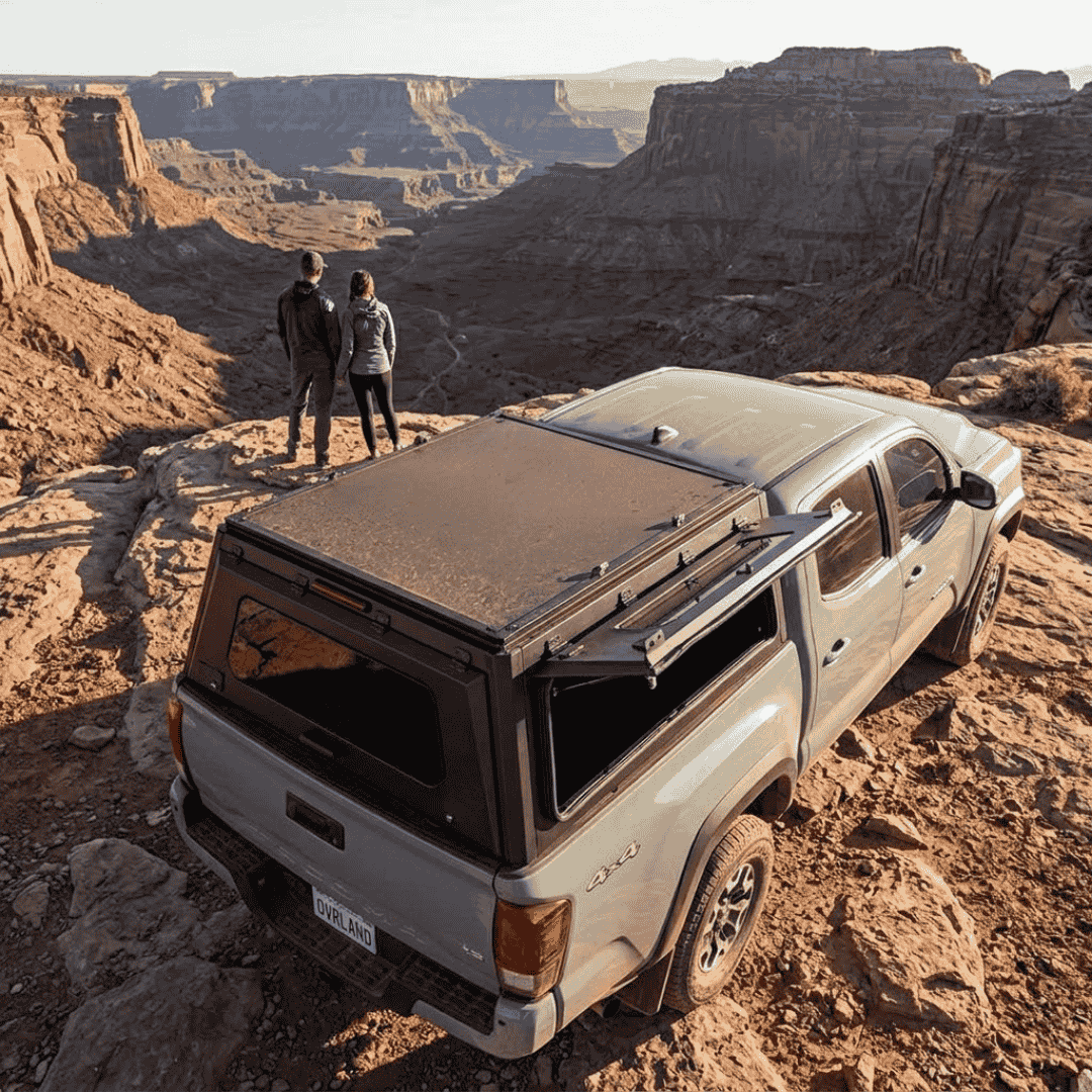 Overland Vehicle Systems Expedition Truck Cap with Sliding Windows for 2016 to 2023 Toyota Tacoma 5 Ft. Bed parked overlooking a canyon with windows open