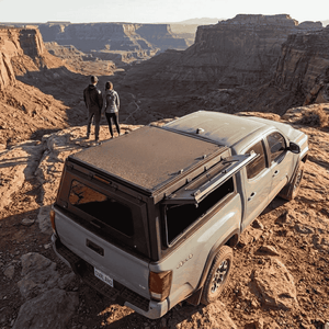 Overland Vehicle Systems Expedition Truck Cap with Sliding Windows for 2016 to 2023 Toyota Tacoma 5 Ft. Bed parked overlooking a canyon with windows open