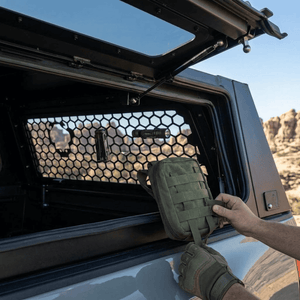 Overland Vehicle Systems Expedition Truck Cap with Sliding Windows for 2016 to 2023 Toyota Tacoma 5 Ft. Bed parked with a man storing a bag through the back window