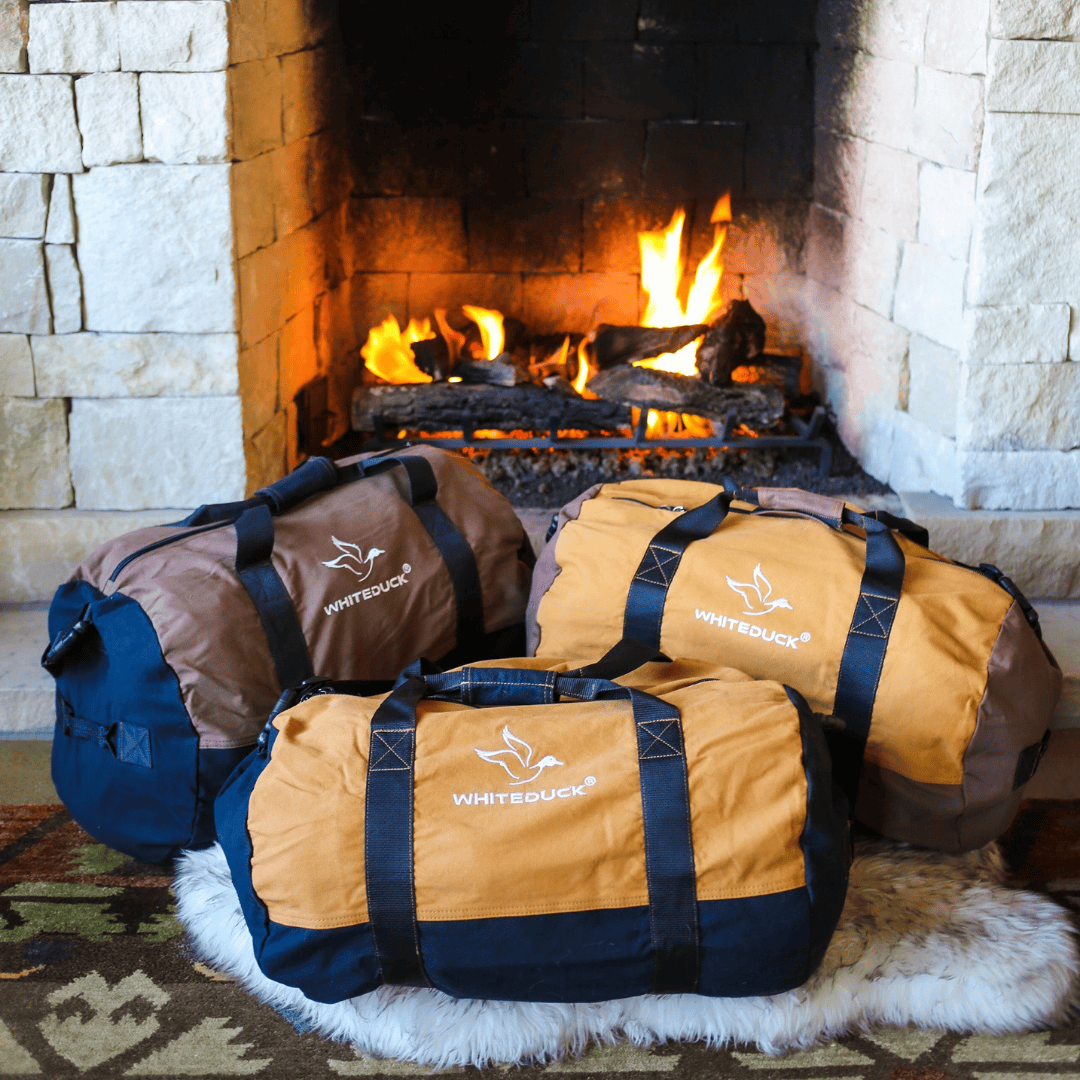 White Duck Outdoors Filios Canvas Duffel Bag bundled in front of a fireplace