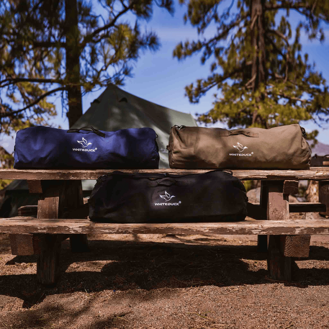 White Duck Outdoors Hoplite Canvas Duffel Bag blue black and olive on bench front view