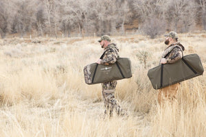 Picture of two bags containing the Disc-O-Bed Cam-O-Bunk Large with Mossy Oak including Organizers being carried by two men.